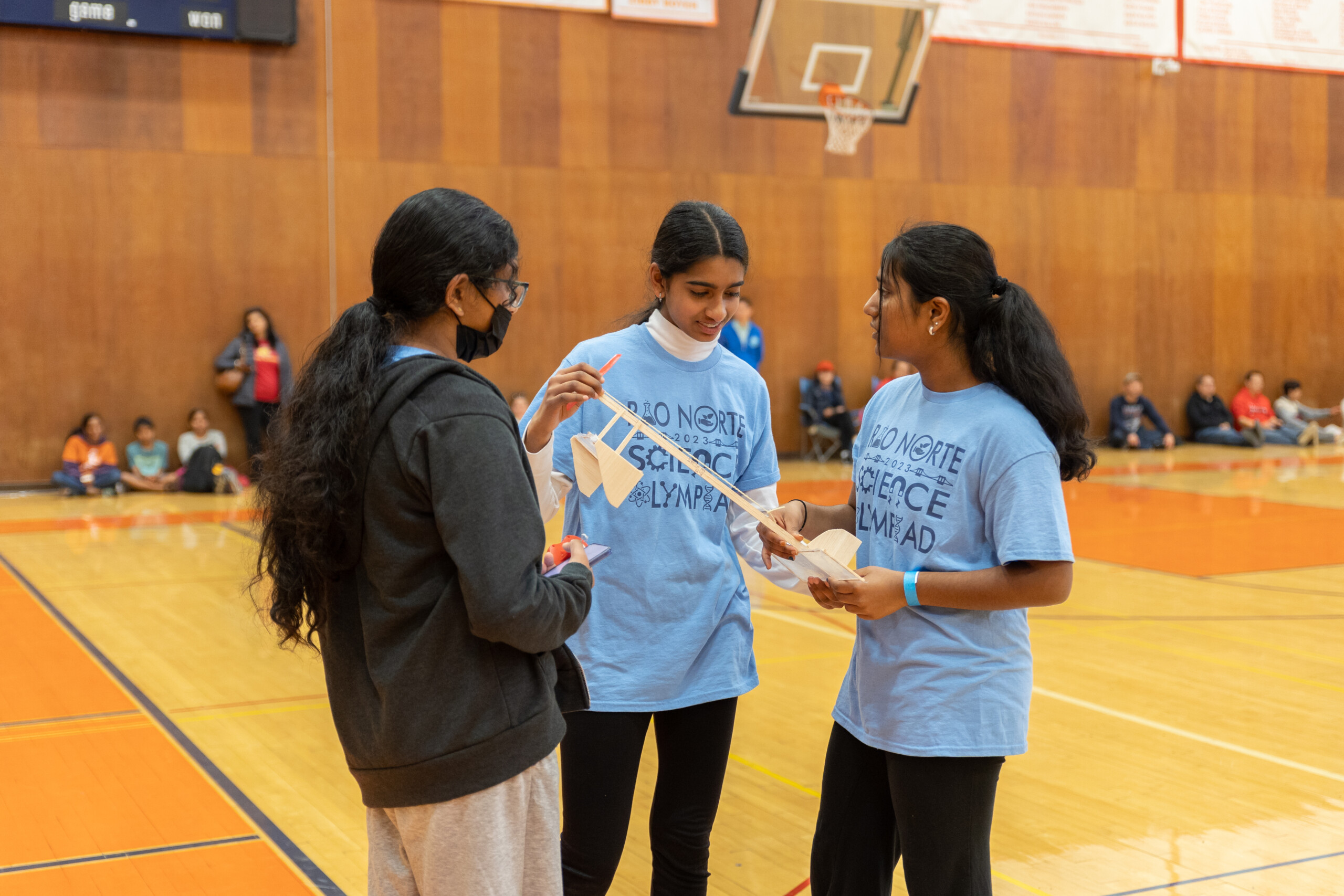 Three young women holding an apparatus and participating in Science Olympiad